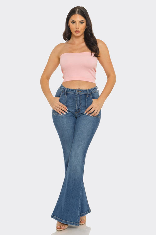 Woman wearing a strapless ribbed bandeau crop top with flared denim jeans, showcasing a stylish outfit.